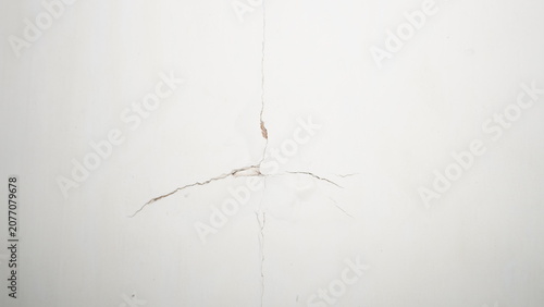 Fotografia Cracked white plaster wall with spreading hairline fractures.