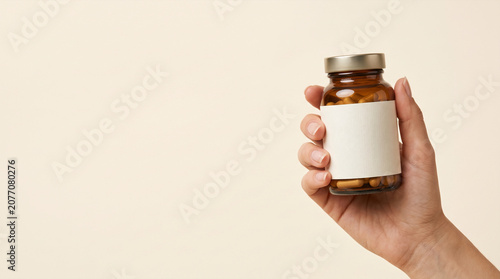 Hand holding amber glass bottle filled with health supplements on plain background