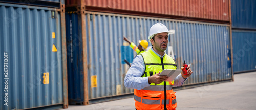 Photos Port worker using a radio transceiver to control a crane loading container boxes