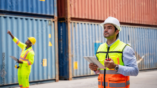 Port worker using a radio transceiver to control a crane loading container boxes onto a cargo ship, representing sea transportation and logistics business concepts