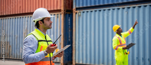 Foto Port worker using a radio transceiver to control a crane loading container boxes
