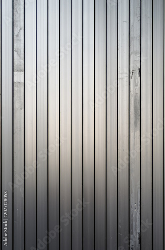 Vertical Metal Slat Wall Texture Background with subtle industrial wear. A pattern of metallic slats or panels with a brushed silver finish and the authentic, non-uniform signs of aging and usage.