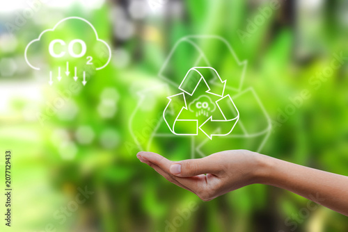 Human hand holding virtual recycling and CO2 reduction icons with  green nature background. Concept for circular economy, carbon reduction, sustainable waste management, and environmental care.