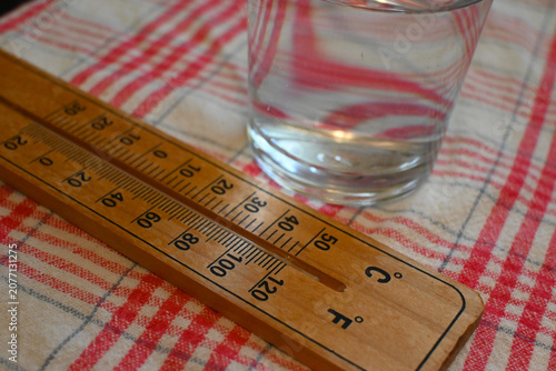 Close-up of a glass of water placed next to a thermometer, representing heatwave at home, hot weather and hydration concept.