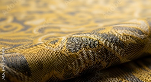 A close-up view of a luxurious golden and dark grey patterned fabric with intricate woven details and a rich texture.