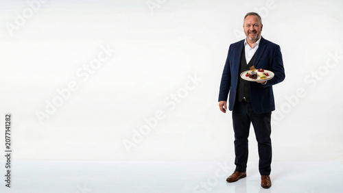 Smiling mature businessman or restaurant manager holding a gourmet dessert plate. Isolated on white background with huge copy space. Perfect for catering and luxury hospitality concepts.
