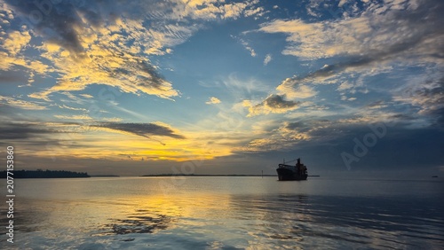 Cargo ship sailing on calm water at sunset with golden sky