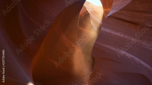 In a Danxia landform canyon, intense afternoon light pierces through the narrow crevices; suspended red-soil dust is drawn into the beams, forming spiraling columns of light that slowly twist