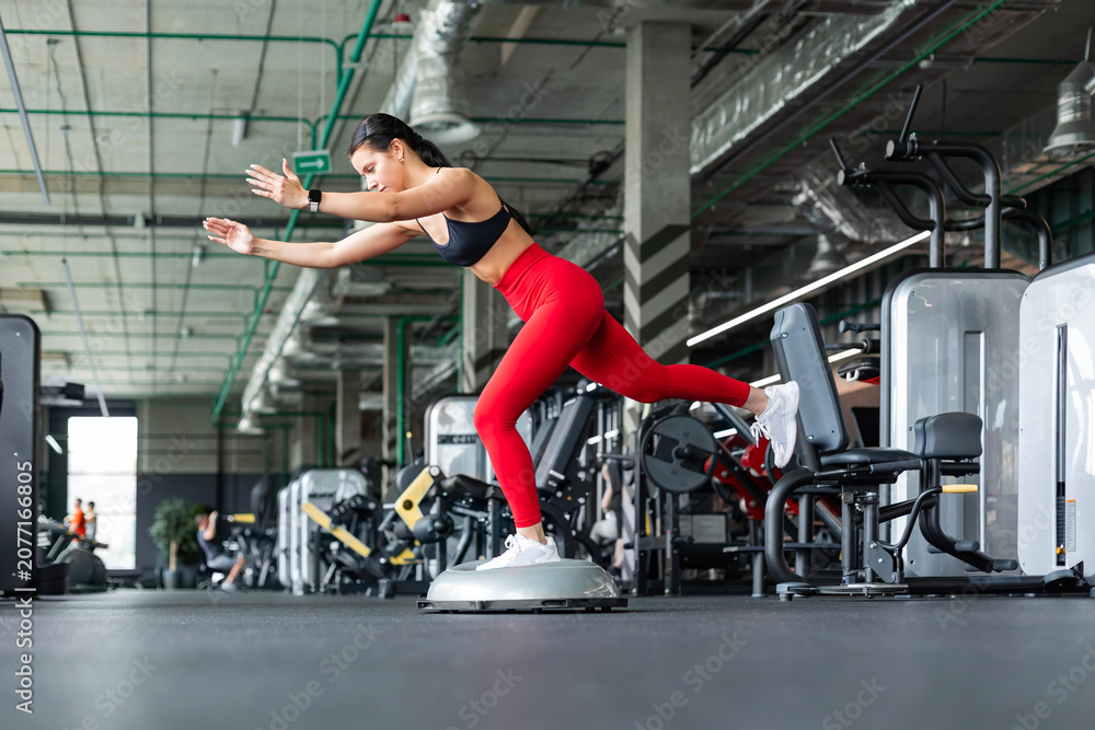 Fototapeta premium Athletic woman doing single-leg deadlift balance exercise on BOSU ball at gym