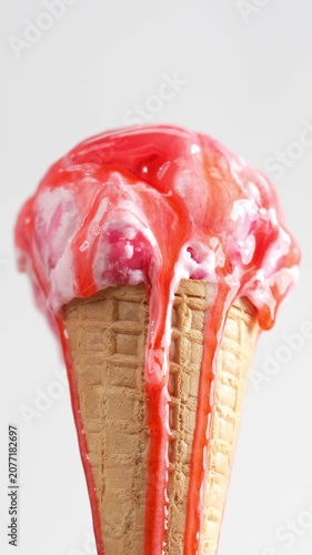 4K Close-up of pink strawberry ice cream cone with sweet red syrup dripping down the sides of the crispy waffle cone, isolated on light neutral background.