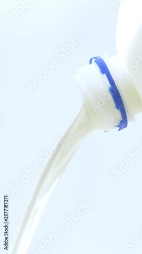 4K Close-up of fresh white milk or cream pouring smoothly from bottle mouth against on white background.
