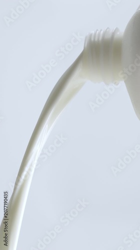 4K Close-up of fresh white milk or cream pouring smoothly from bottle mouth against on white background.