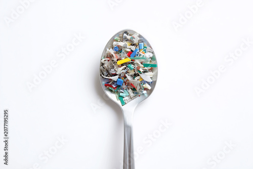 A spoon filled with colorful plastic debris, against a white background, top view.