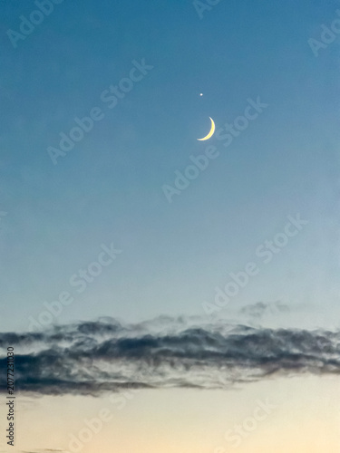 Crescent moon and Venus conjunction in twilight blue sky above soft clouds at dusk in Antwerpen, België