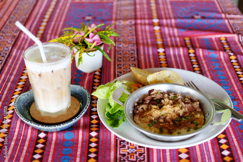 Fresh egg omelet and Minced pork in a frying pan with garlic bread and vegetables in white plate. A clear glass of iced latte coffee with flower vase on the table