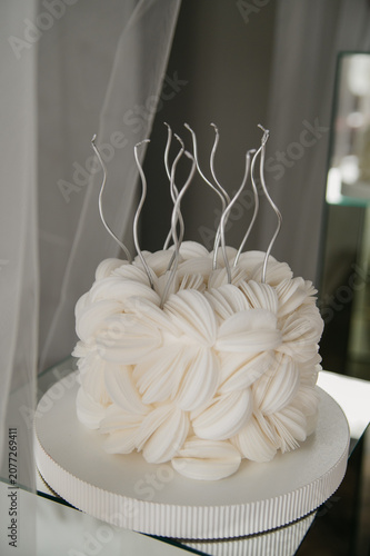 A strangely shaped birthday cake with candles on top stands on a table for a birthday celebration, with white tulle hanging in the background