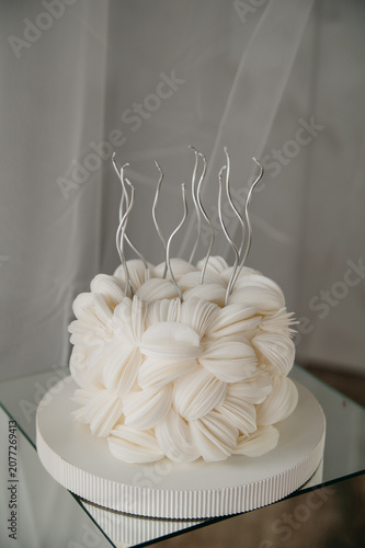 A birthday cake with candles stands on a table, with white tulle hanging in the background
