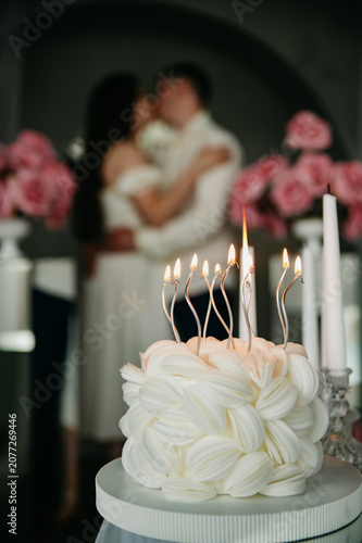 Young couple in love kissing in a photo studio during a birthday or wedding anniversary celebration in front of a sweet cake with candles in it