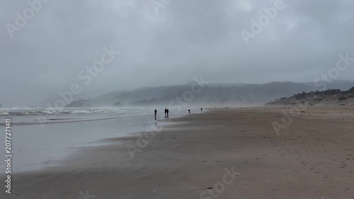 4K smooth action camera footage of stormy Cannon Beach in summer, Oregon, USA, with Haystack Rock, crashing Pacific Ocean waves, rain, mist and visitors exploring the coastline.