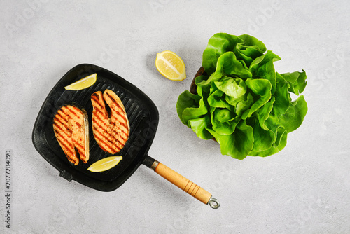 Foto Grilled salmon steak on griddle pan with fresh butterhead lettuce and lemon on g