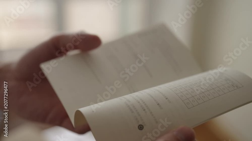Close-up of hands flipping through Japanese manual and pointing to checklist grid on page, suggesting focused studying, reviewing instructions and reference material. Shooting in slow motion
