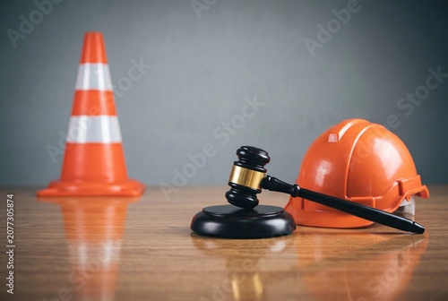 Wooden gavel resting on a hard hat next to a traffic cone representing legal issues and safety regulations in the construction industry on a wooden desk