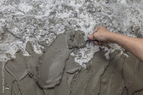 Hand presses wet concrete into rough surface. Texture contrasts show grit and smoothness. Worker molds material with focused effort. Ideal for construction, renovation, or DIY projects