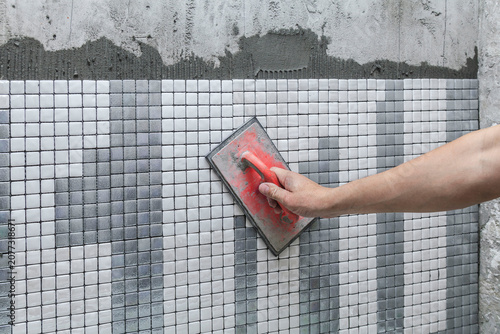 Hand smooths tile adhesive with a red sponge