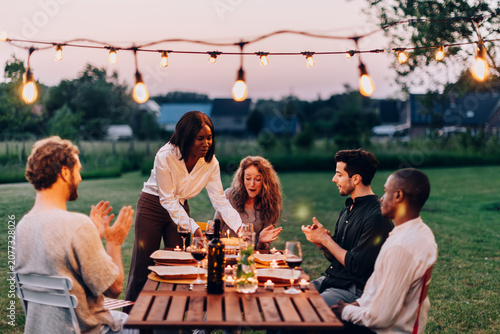 Friends celebrating birthday at outdoor dinner party with string lights
