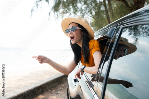 A joyful traveler is feeling the coastal breeze as she drives her SUV. Dressed in a chic sun hat and sunglasses and the calm ocean backdrop completing this perfect getaway