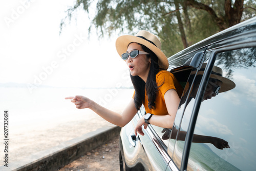A joyful traveler is feeling the coastal breeze as she drives her SUV. Dressed in a chic sun hat and sunglasses and the calm ocean backdrop completing this perfect getaway