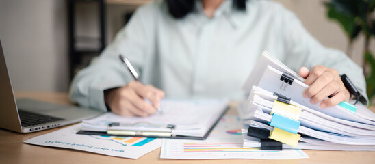 Business professional reviewing performance reports and auditing stack of documents at office desk. Concept of corporate audit, compliance check, data analysis,