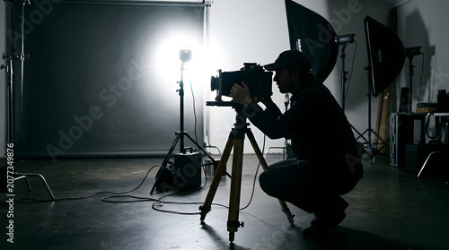 A photographer adjusts camera settings on a tripod in a studio.