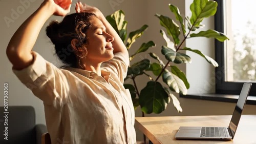 Relaxed woman stretching by laptop in sunny home office