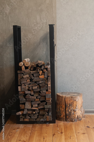 Stacked firewood in black metal rack and wooden stump