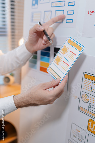Photography Close-up of a UX designer reviewing wireframes, interface layouts, and visual design elements on a planning board for user interface development, usability testing, and digital product design