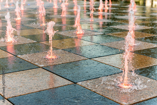Tableau sur toile Pink tinted water jets in urban square fountain