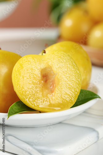 Картината върху платно Fresh Golden Yellow Plums Cut in Half on White Plate with Green Leaves