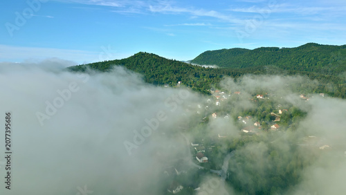 Photography An aerial view captures a serene landscape with dense forest and mist-covered clouds, highlighting the peaceful coexistence of nature and human habitation