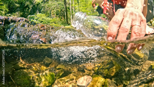 Photos A caucasian woman enjoying a hike in a lush forest, captures the purity of flowing water in a clear bottle