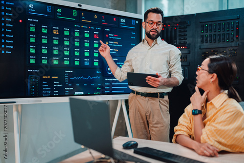 Tableau sur toile It professional explaining server rack alert status on a dashboard to a female c