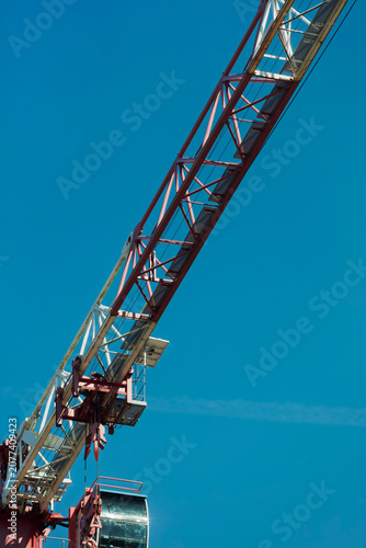 Konstfotografi The long steel jib of a tower crane stretches diagonally across a clear blue sky over a city construction site