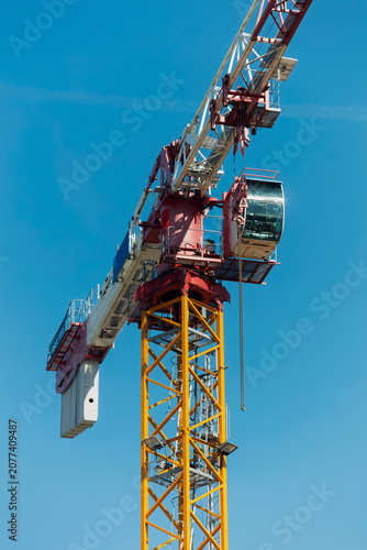 Schilderij op canvas Close-up of a tower crane operator cabin and counterweight high above a construction site against a deep blue sky