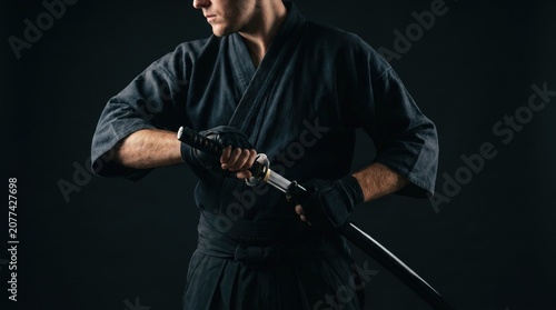 Modern Samurai Warrior Drawing a Sharp Katana Sword in Black Martial Arts Uniform Against Dark Background