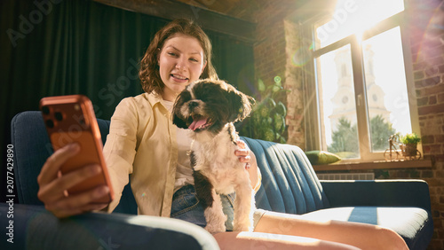 Foto Young woman taking cheerful selfie with small dog in cozy home