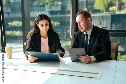 Картината върху платно Business professionals discuss project details while comparing tablet with printed documents inside modern office