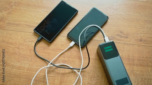 Dual smartphone charging from power bank using connected cables portable battery in operation. Screen presenting bar style charge indicators for each output channel instead of percentage values