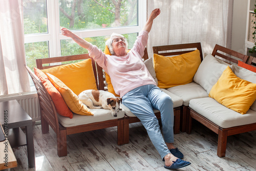 Quadro su tela Senior woman stretching on sofa with dog at home