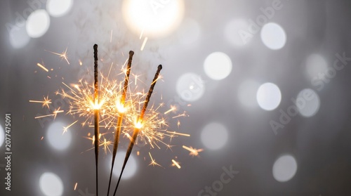 Three burning sparklers against a blurred background with bokeh lights