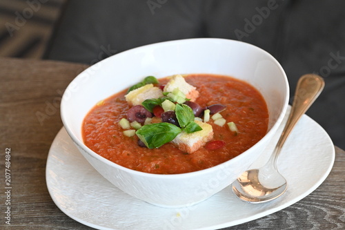 Gazpacho served with avocado and olives in a white bowl, top view of an elegant restaurant dish on a rustic wooden table, fresh Spanish cuisine, colorful food presentation and culinary background